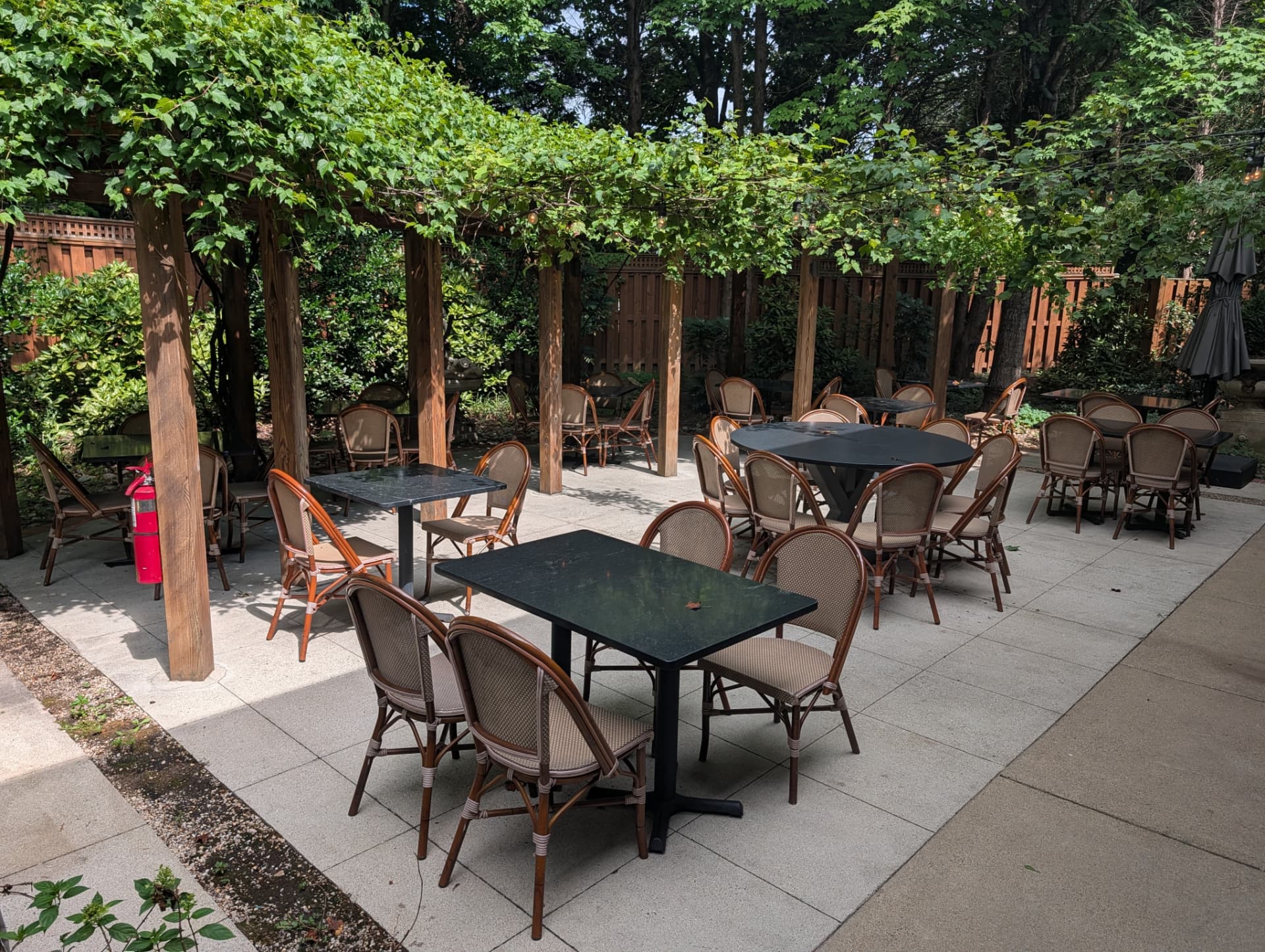 Garden patio with tables and bistro chairs beneath a vine-draped pergola