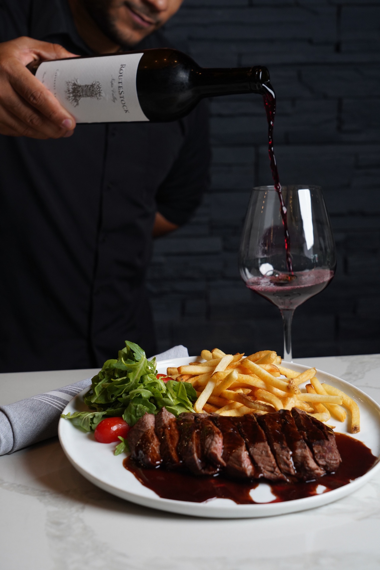 Steak frites with a green salad and red wine being poured into a glass